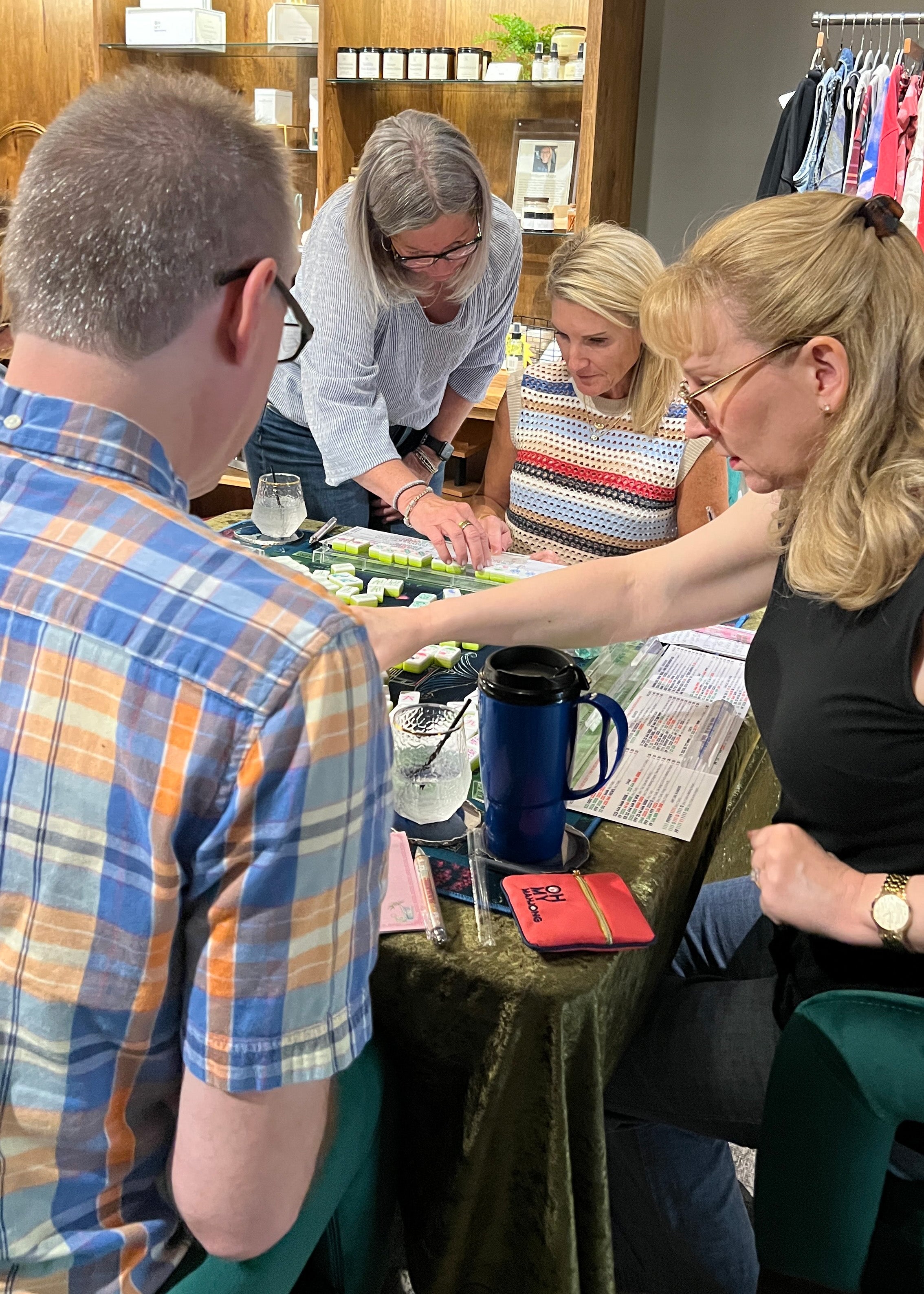 Group of people gathered around a mahjong table in a store setting.
