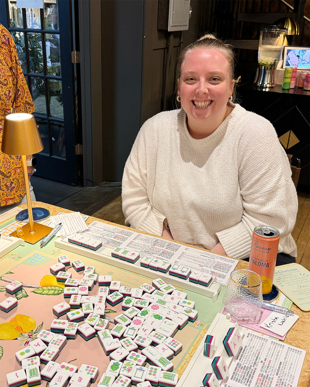 Person sitting at a table with mahjong table, smiling.