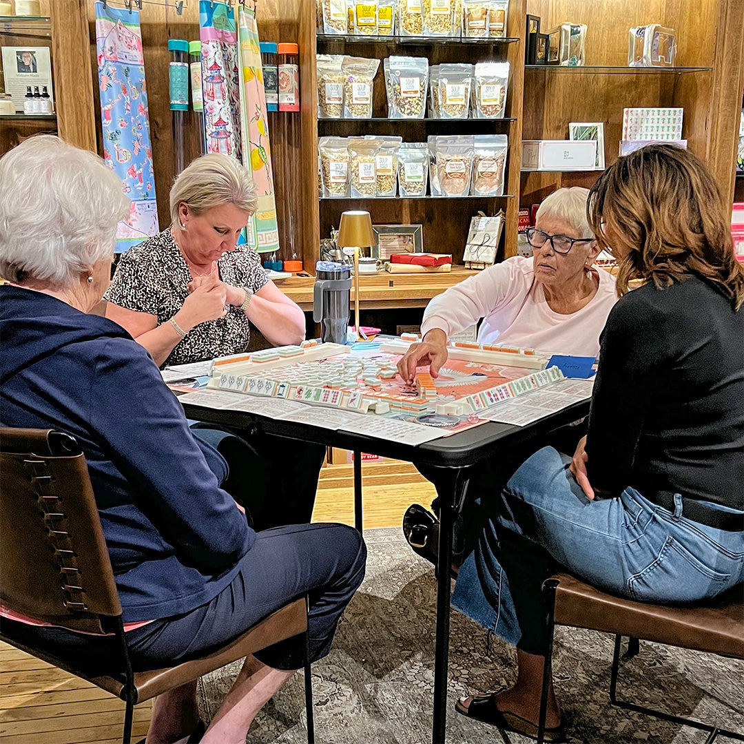 Four women playing mahjong together in a store setting.